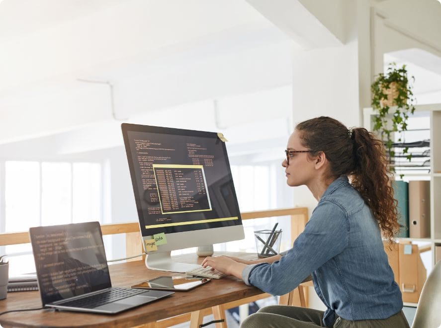 side-view-portrait-female-it-developer-typing-keyboard-with-black-orange-programming-code-computer-screen-laptop-contemporary-office-interior-copy-space
